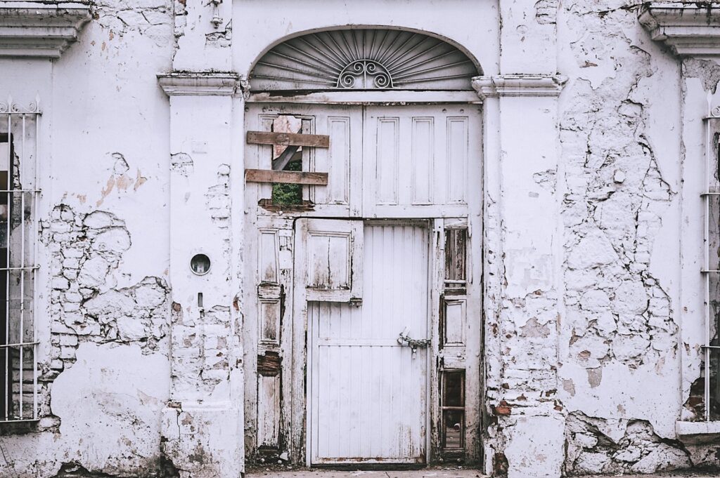 An old, decaying white building with a weathered door and cracked walls.