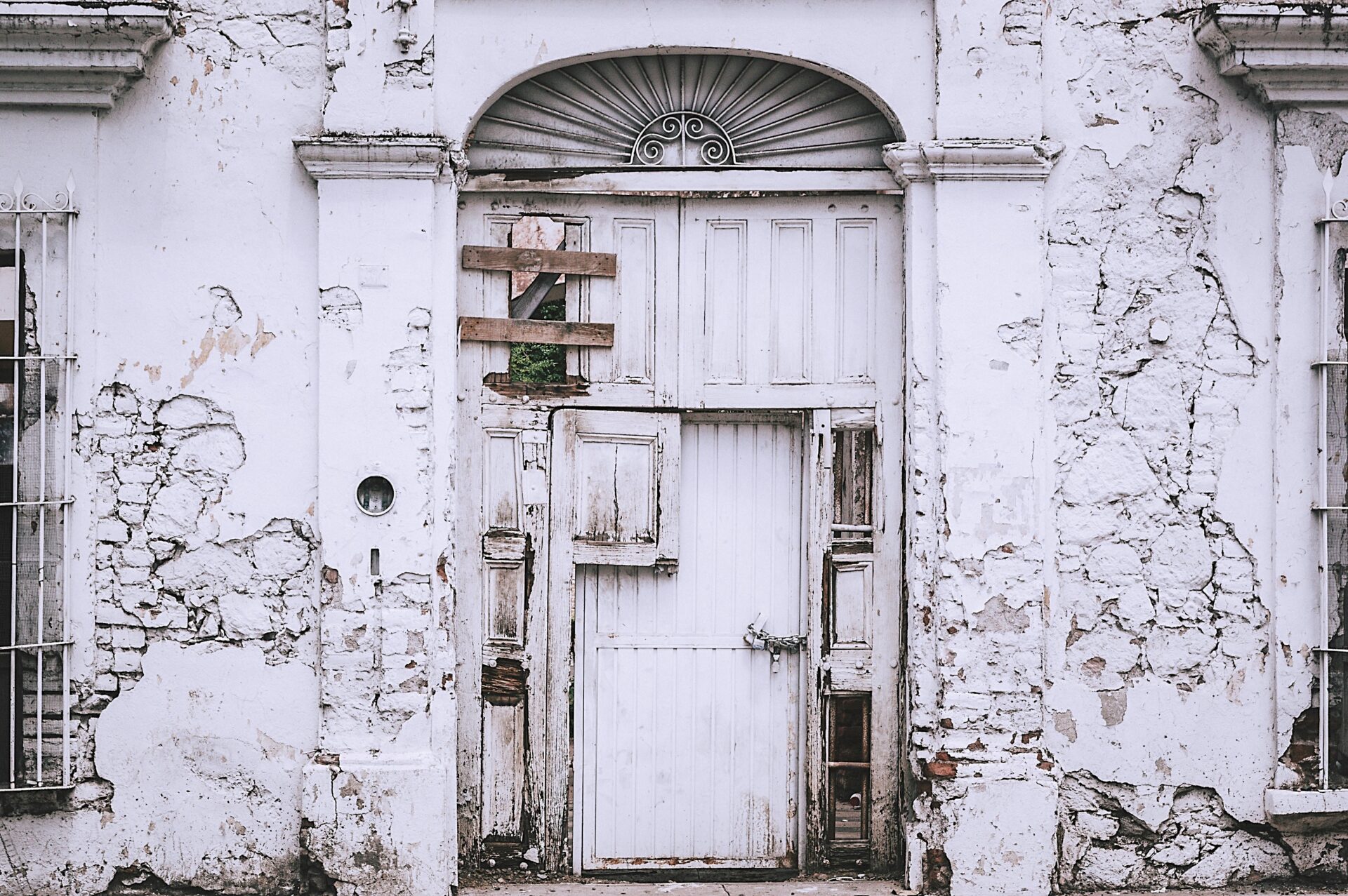 An old, decaying white building with a weathered door and cracked walls.