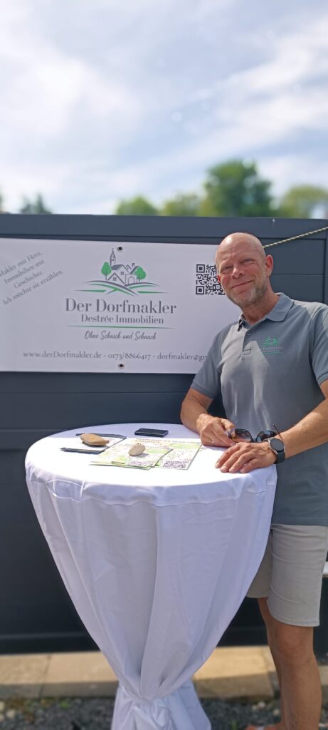 Makler steht am Stehtisch vor einem werbebanner